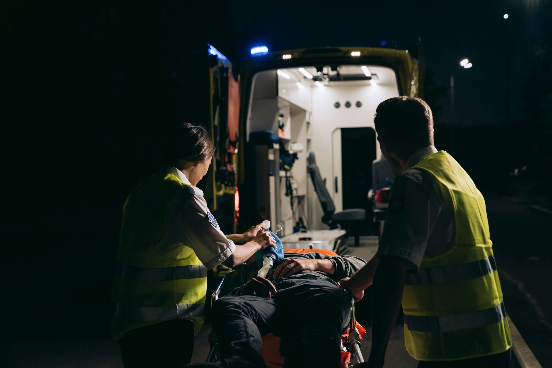 Emergency responders load a person onto a stretcher into an ambulance at night.