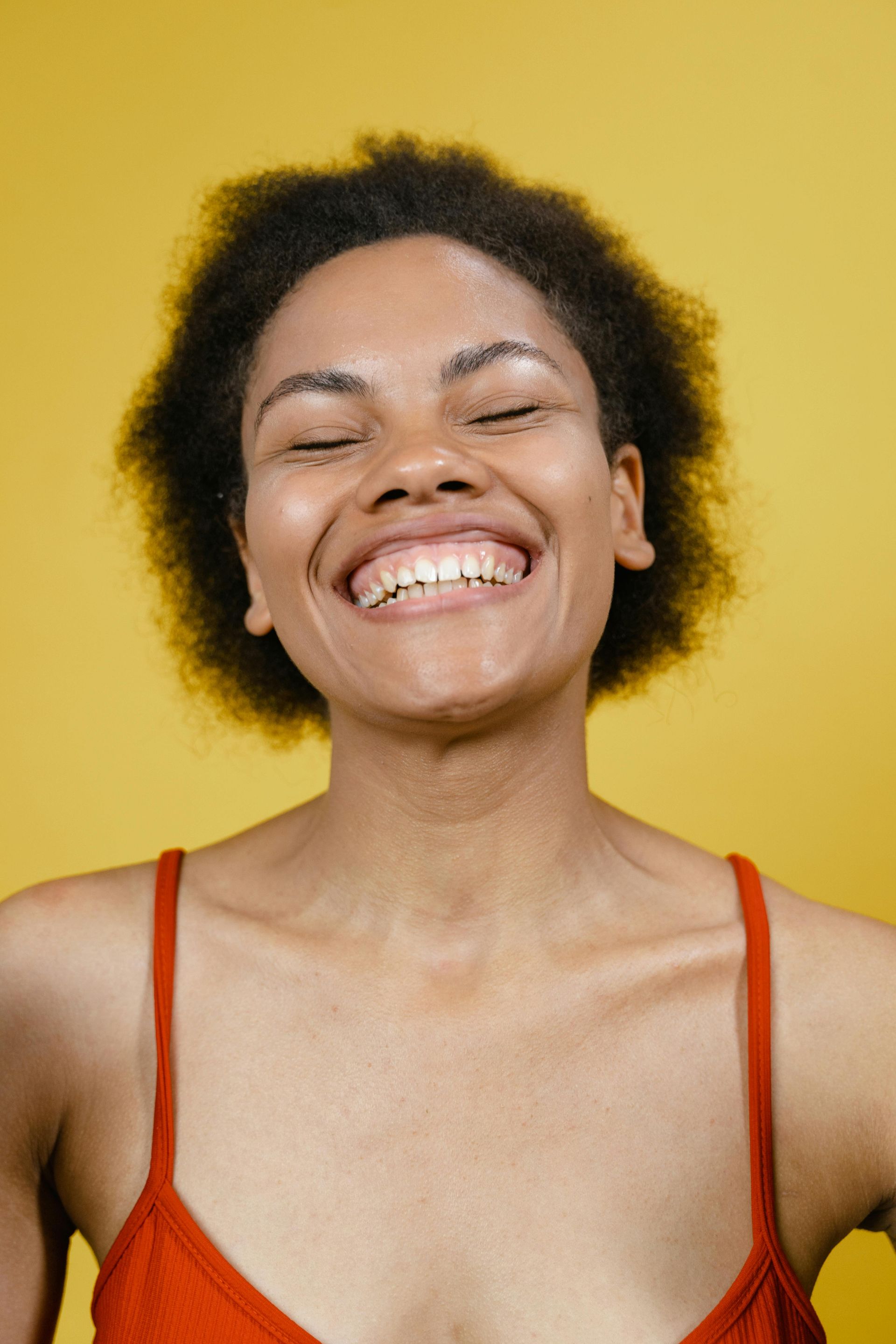 A woman in a red tank top is smiling with her eyes closed.