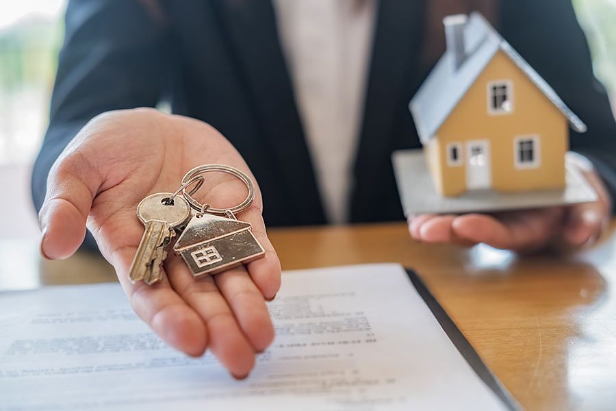 Persona che tiene in mano delle chiavi e una casa in miniatura sopra un documento su un tavolo, probabilmente una transazione immobiliare.