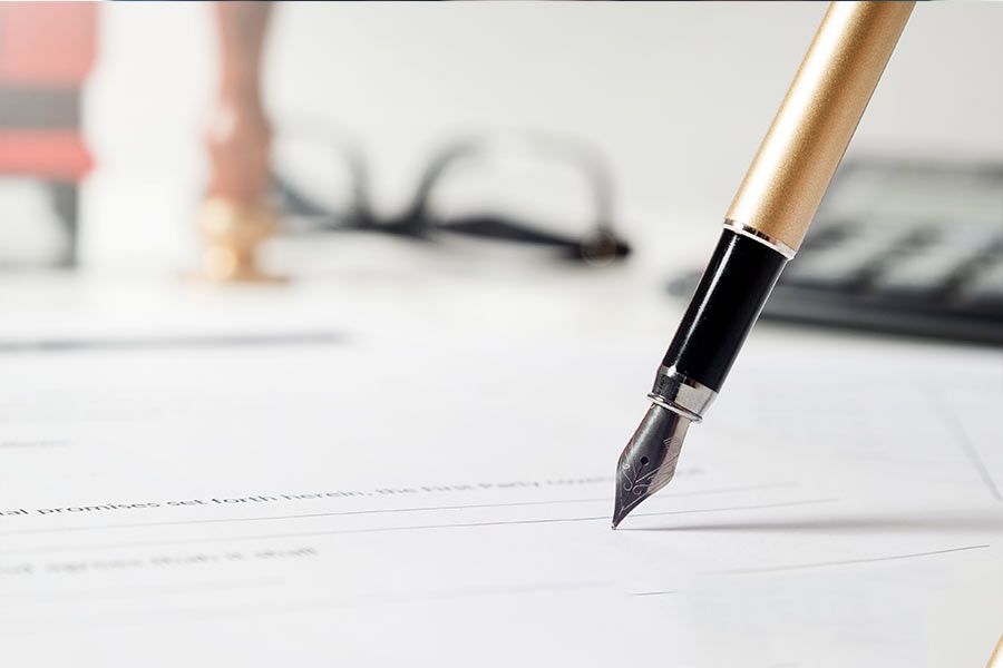 Penna stilografica pronta a firmare un documento; sullo sfondo un paio di occhiali e una calcolatrice.