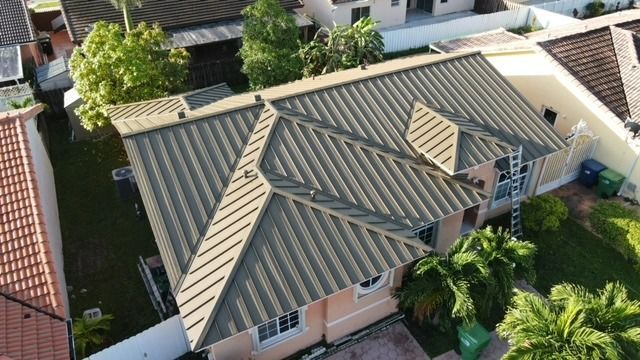 High-angle view of a house with a tan metal roof in a residential area.