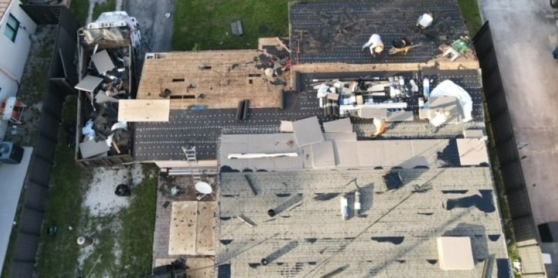Aerial view of damaged roofs and construction workers. Debris scattered, possibly after a storm.