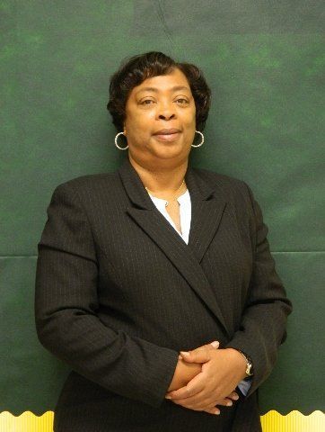 A woman in a black suit is standing in front of a green board