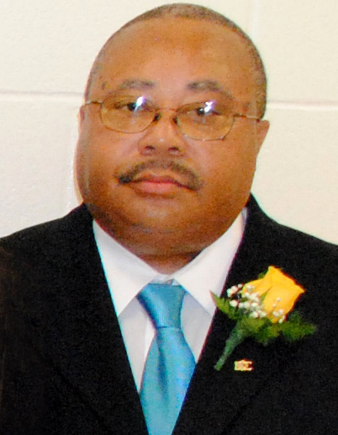 A man in a suit and tie with a yellow rose on his lapel