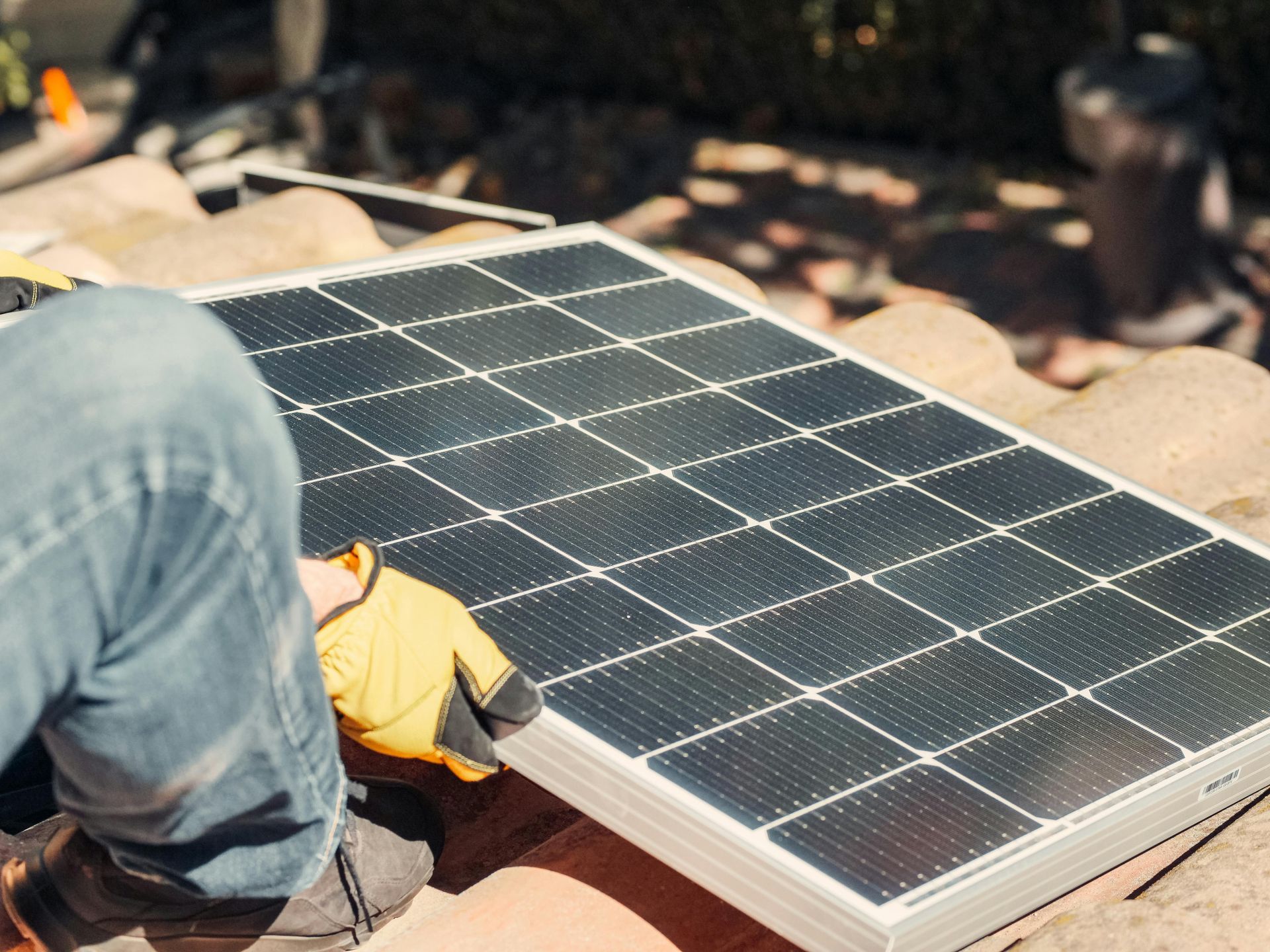 Person in yellow gloves installing a solar panel on a rooftop.