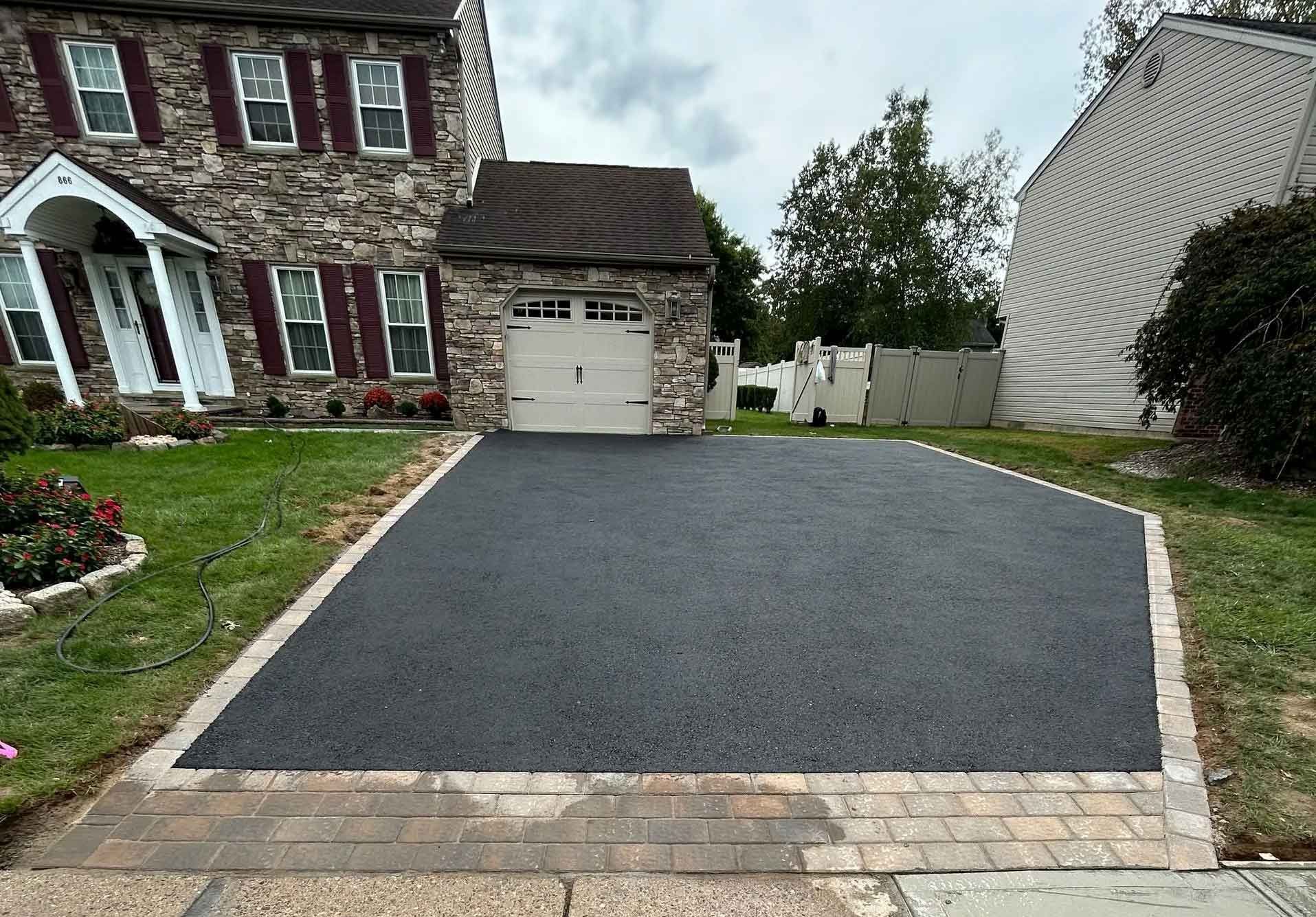 A paved pathway winds through a wooded area with gravel shoulders on both sides, framed by trees and dense greenery.