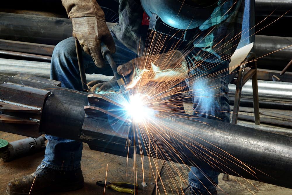 A Man is Welding a Metal Pipe in a Factory — Riverside Aluminium & Stainless in Coolongolook, NSW