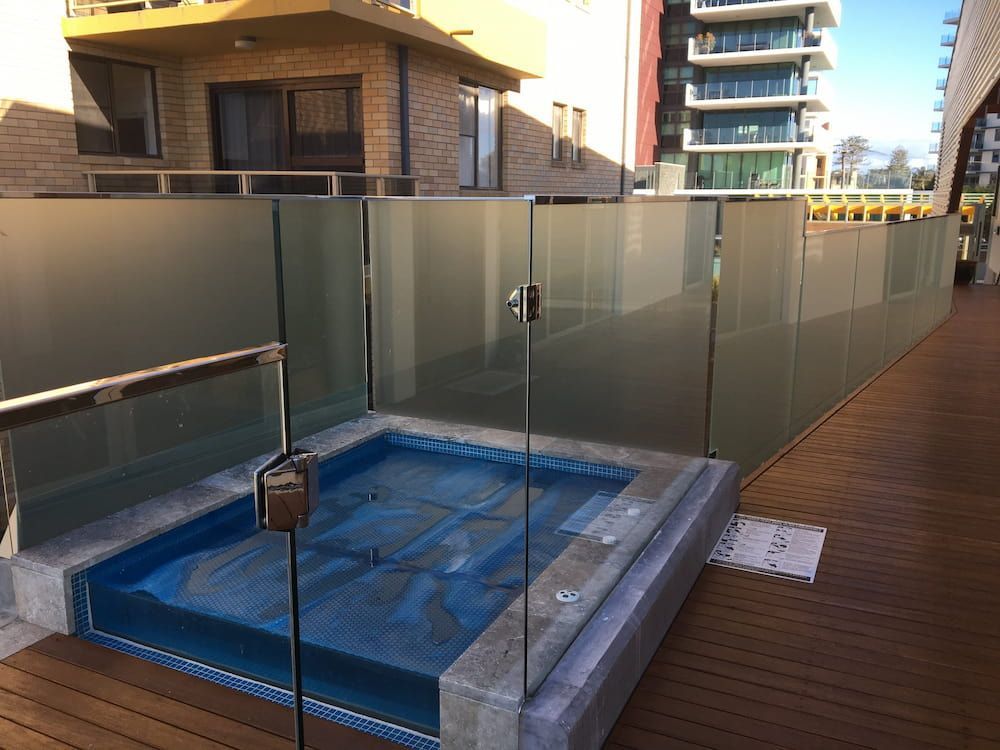 A Hot Tub is Surrounded by a Glass Fence on a Balcony — Riverside Aluminium & Stainless in Forster, NSW