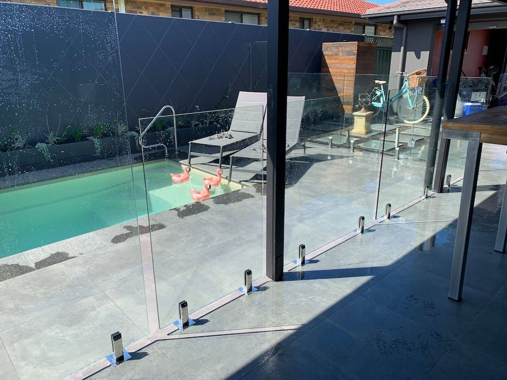 A Swimming Pool With a Glass Fence Around It — Riverside Aluminium & Stainless in Coolongolook, NSW