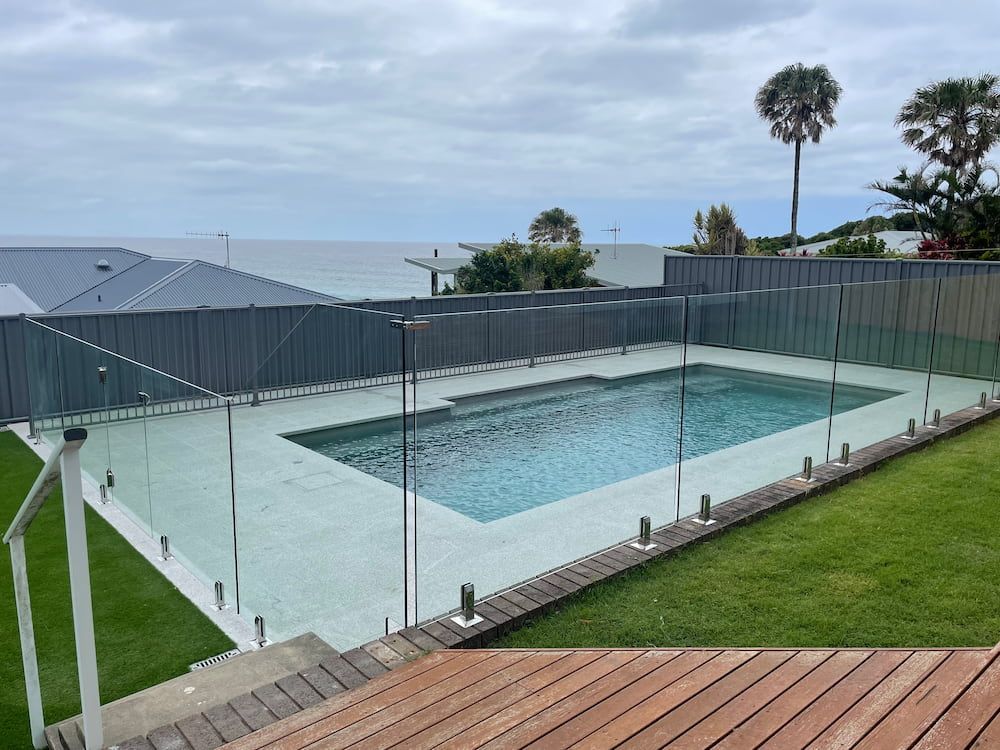 A Large Swimming Pool Surrounded by a Glass Fence With a View of the Ocean — Riverside Aluminium & Stainless in Coolongolook, NSW