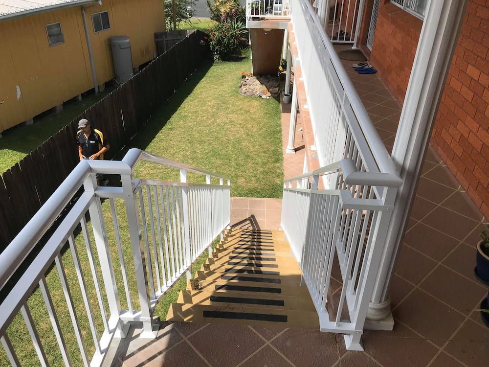 A Man is Standing on a Balcony Next to a Set of Stairs Leading Up to a House — Riverside Aluminium & Stainless in Harrington, NSW