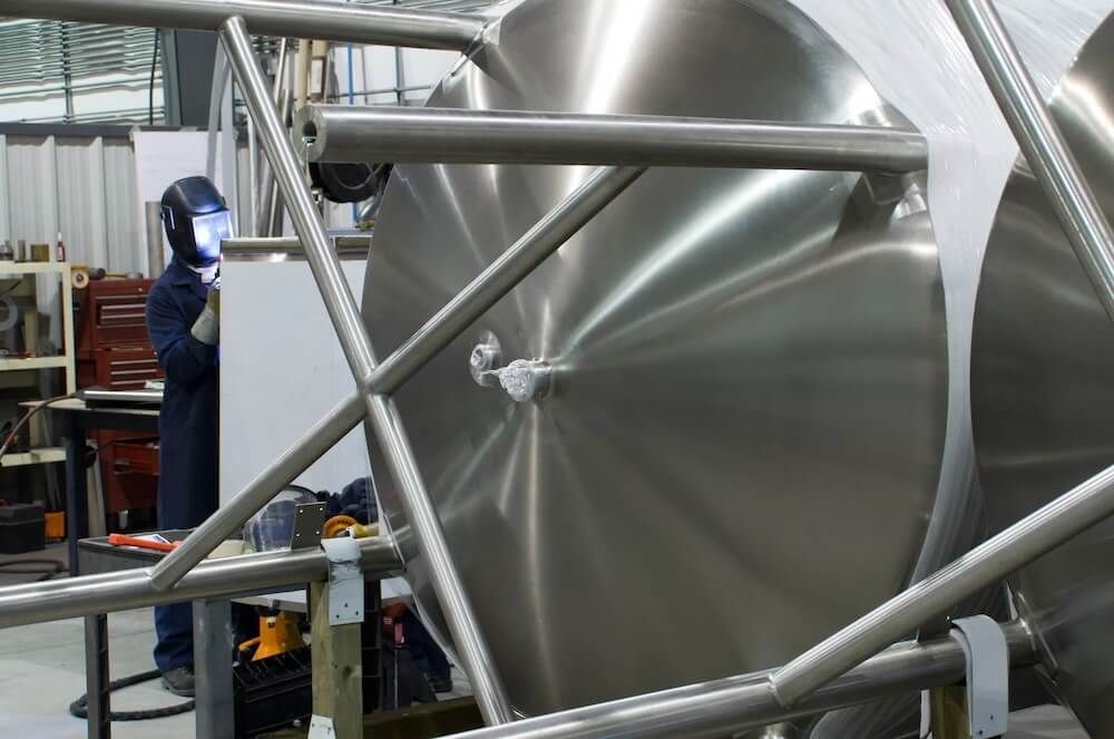 A man is welding a large metal object in a factory — Riverside Aluminium & Stainless in Taree, NSW
