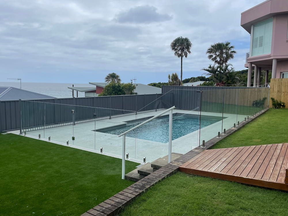 A Large Swimming Pool Surrounded by a Glass Fence in a Backyard — Riverside Aluminium & Stainless in Harrington, NSW