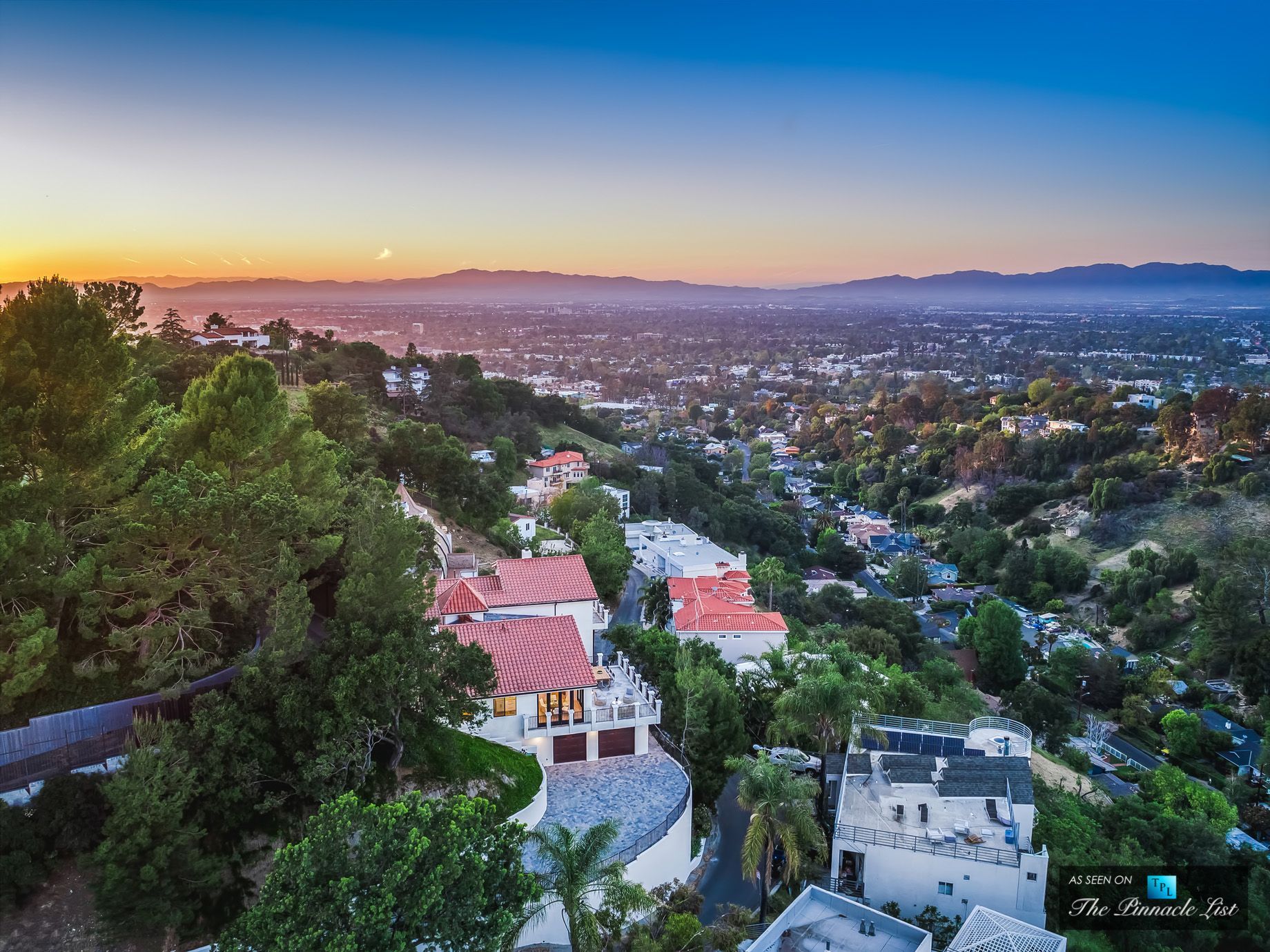 Aerial view of houses nestled in green hills under a colorful sunrise sky.