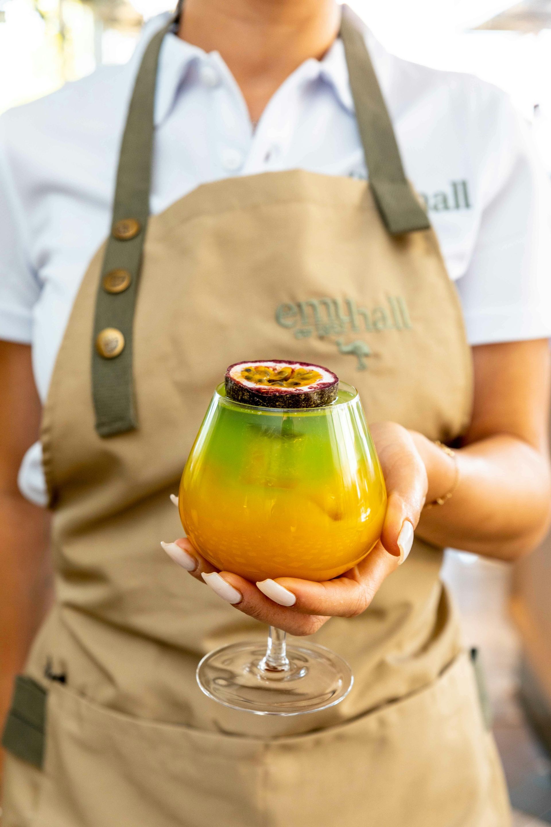 A woman in an apron is holding a cocktail in her hand.