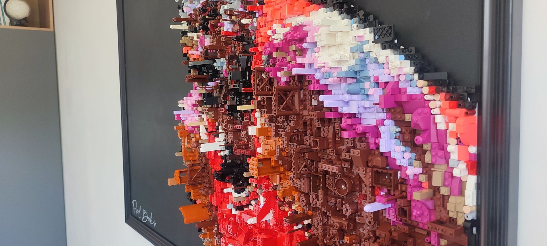 Œuvre d'art abstraite aux couleurs et textures variées, placée dans un cadre noir sur un mur blanc.