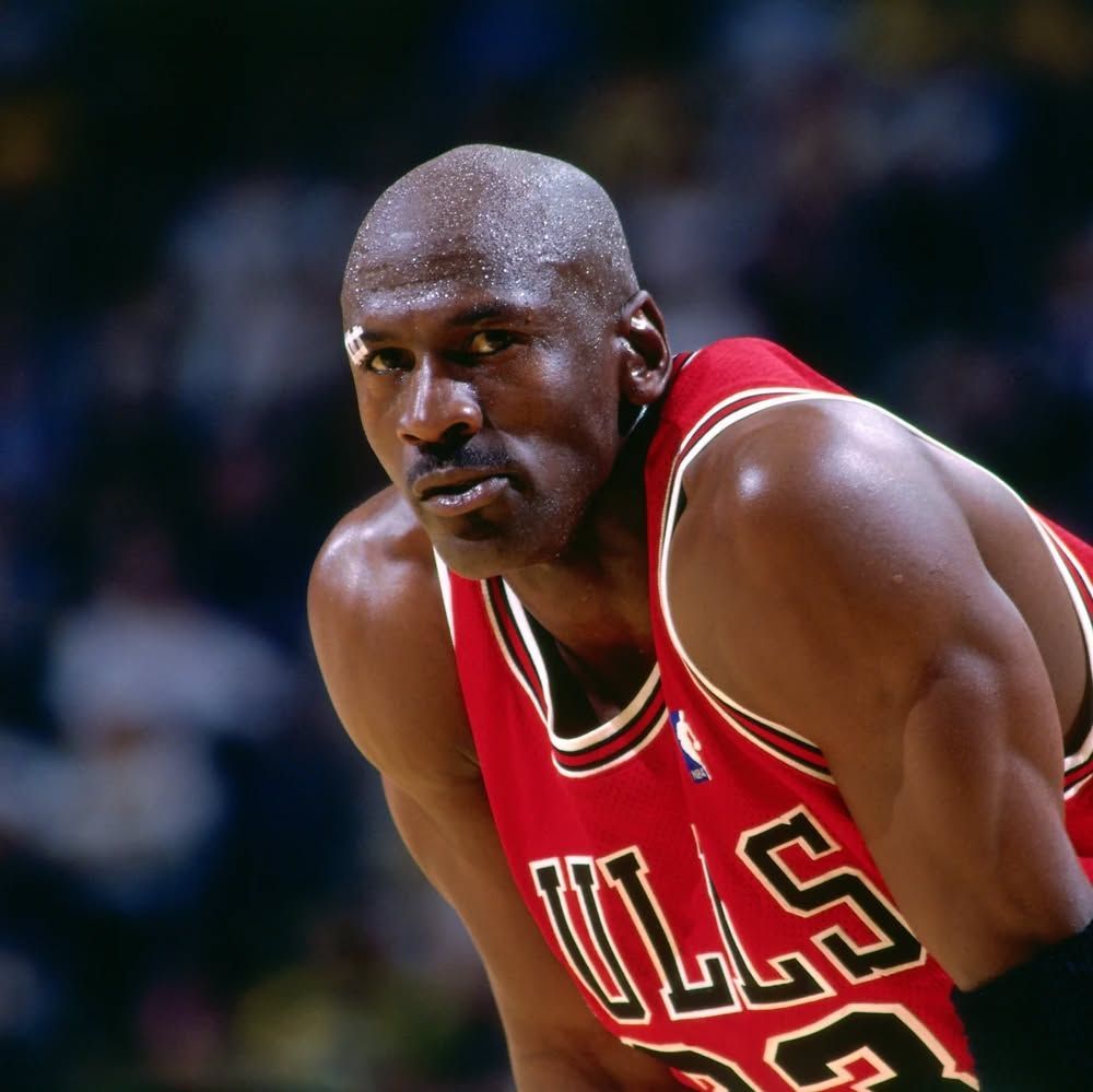Michael Jordan dans un maillot rouge des Chicago Bulls, l'air concentré, en sueur, sur le terrain.