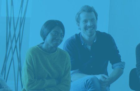 African American woman sitting next to a white man, both smiling and listening to a talk.