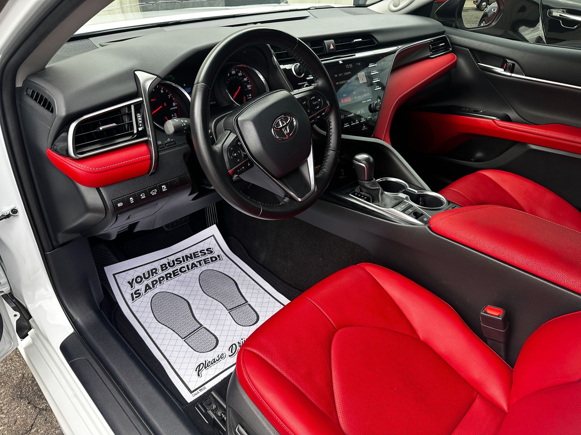 Red and black Toyota Camry interior; seats, dashboard, and steering wheel visible. White floor mat.