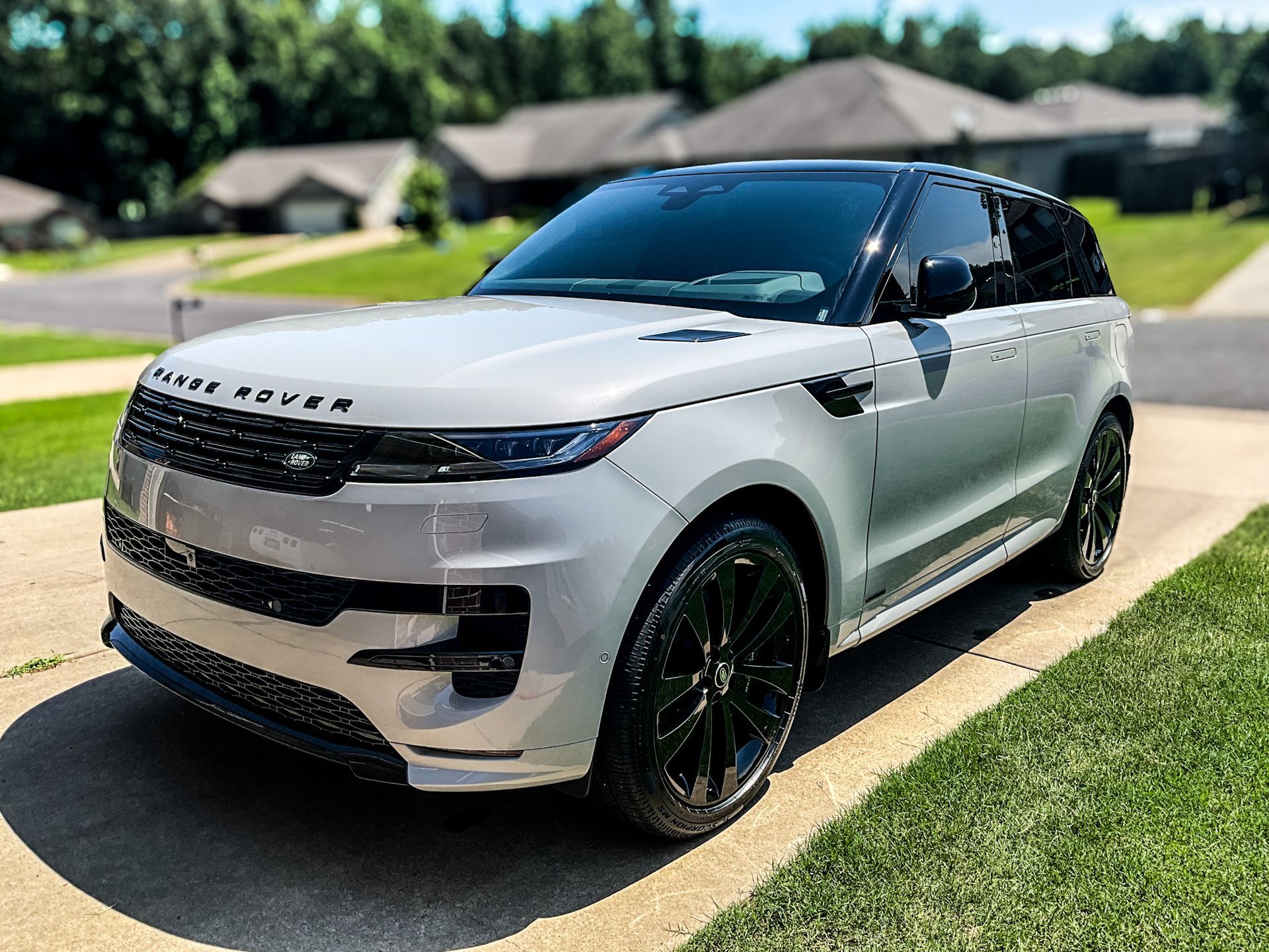 Silver Range Rover Sport SUV parked on a driveway, black wheels, houses in the background.