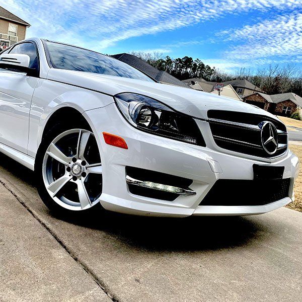 White Mercedes-Benz parked on a driveway under a partly cloudy sky.