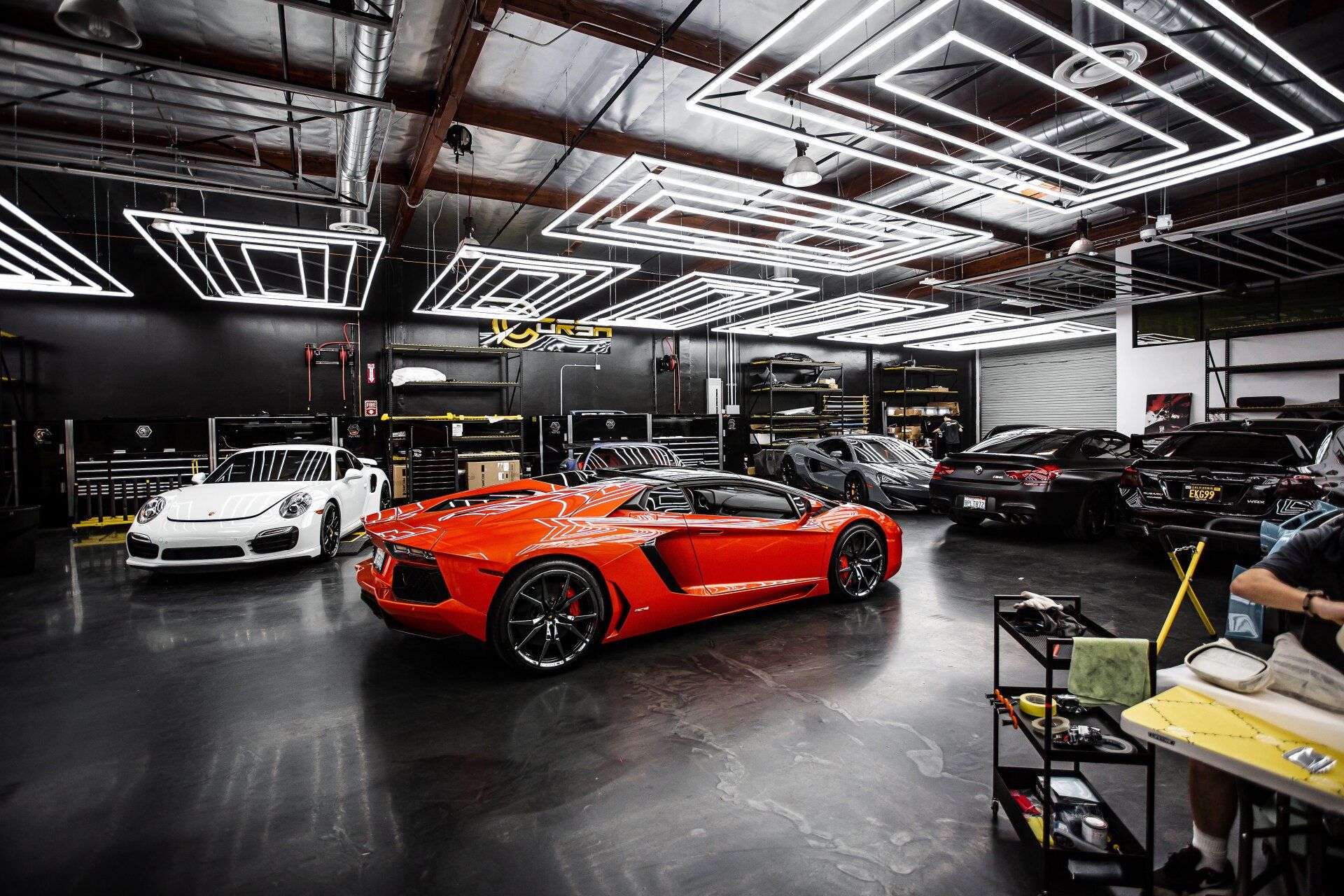 Red Lamborghini and white Porsche in a detailing garage with bright overhead lights.