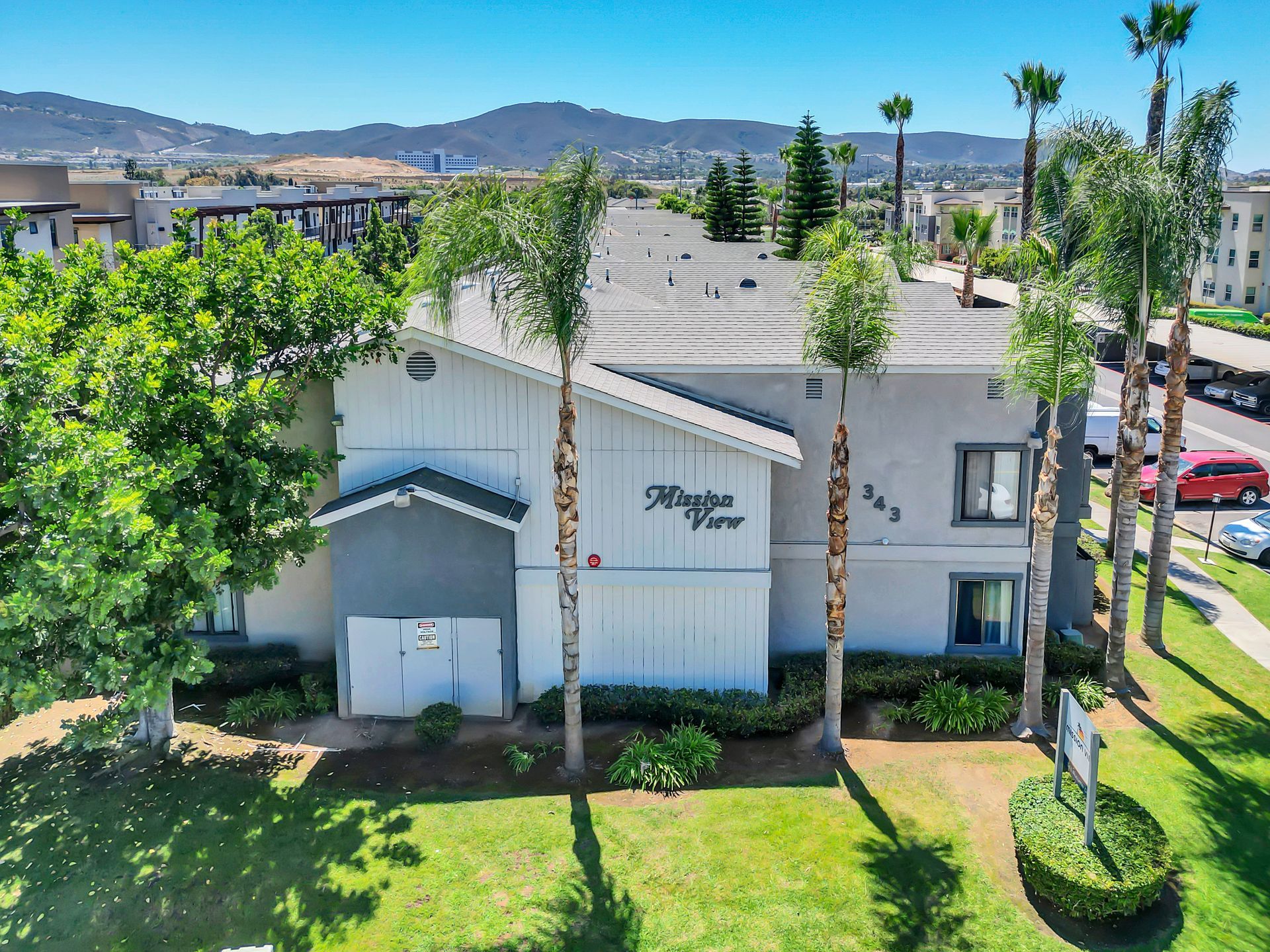 An aerial view of a white apartment building with palm trees in front of it