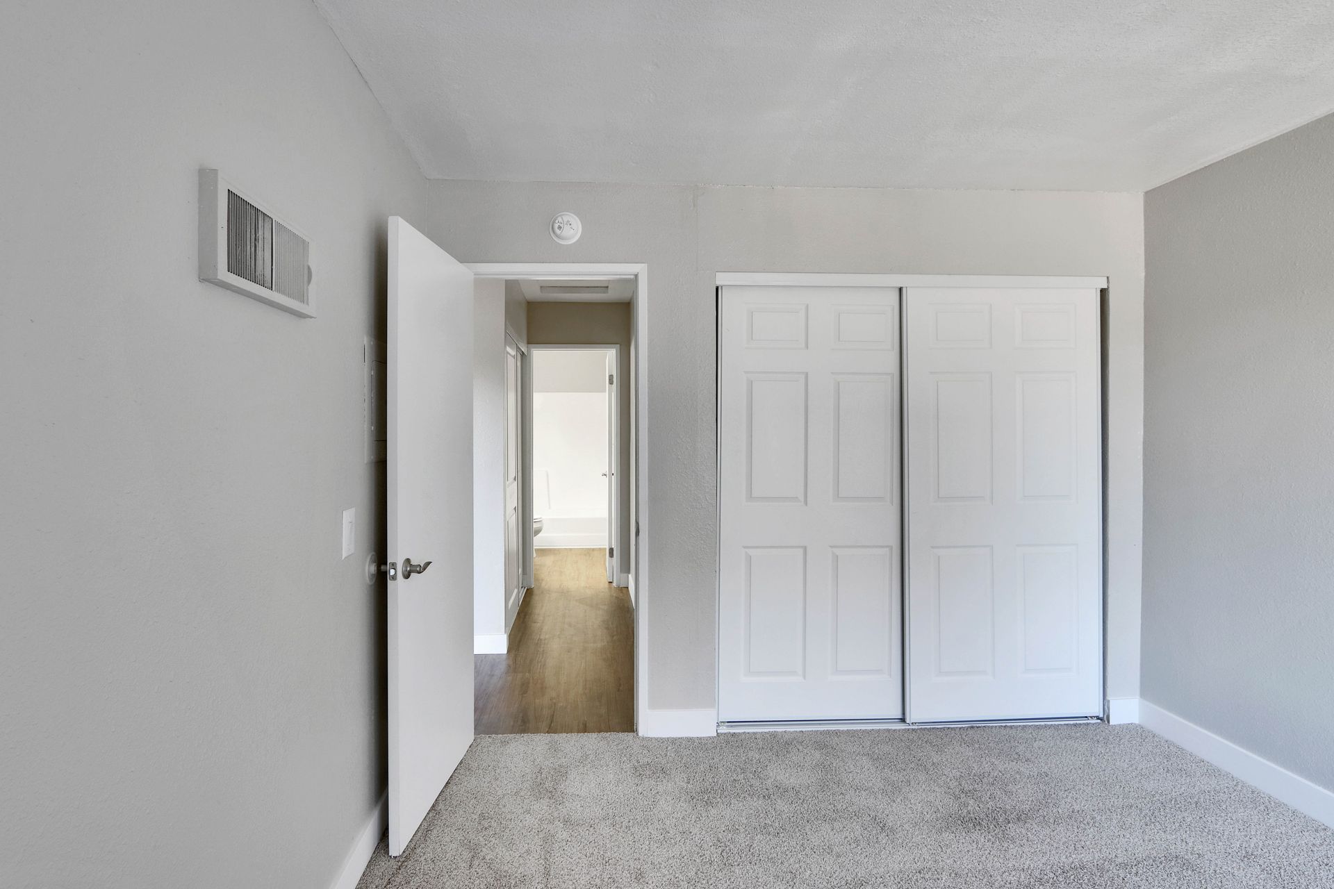 An empty bedroom with sliding closet doors and a carpeted floor.