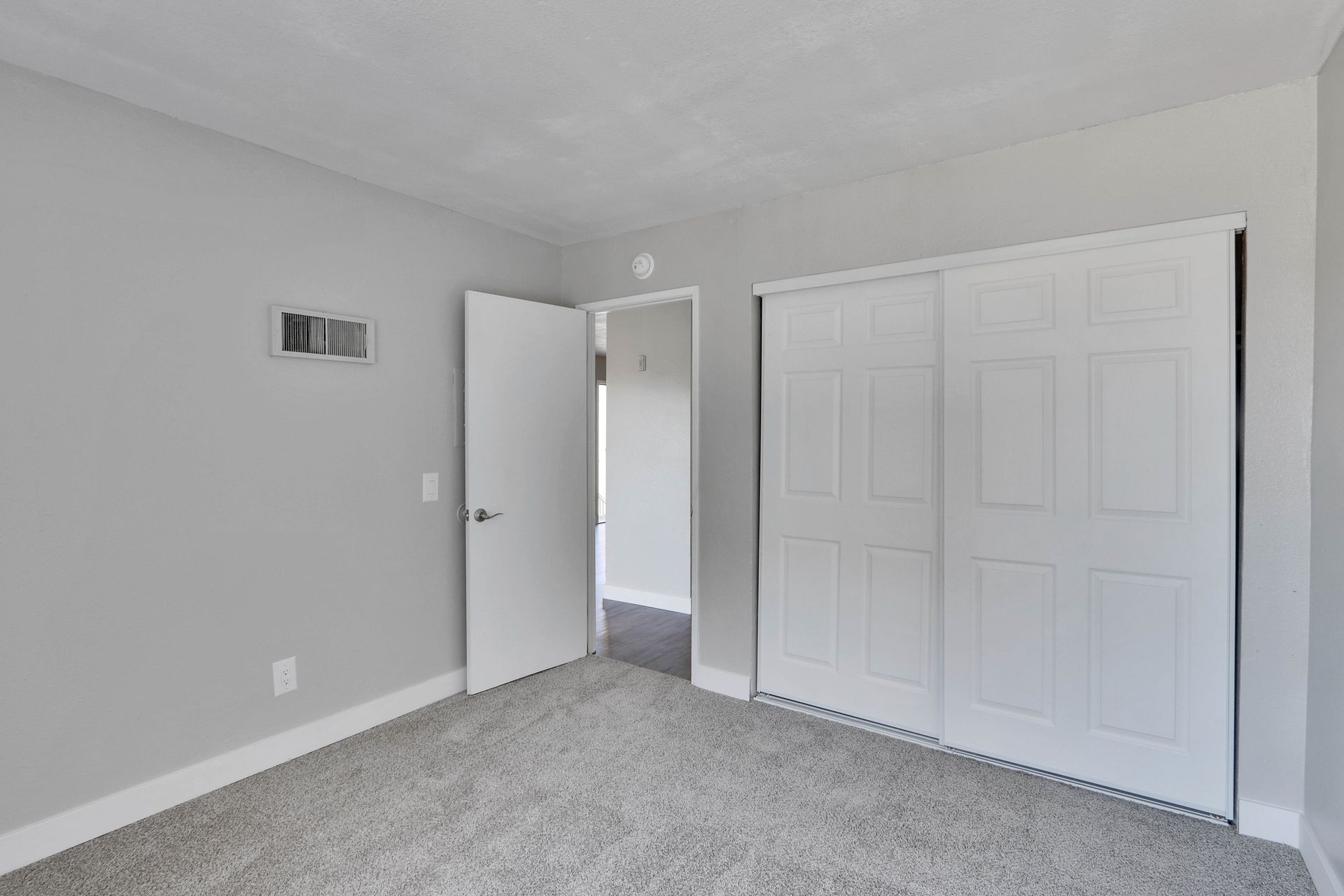 An empty bedroom with sliding closet doors and a carpeted floor.