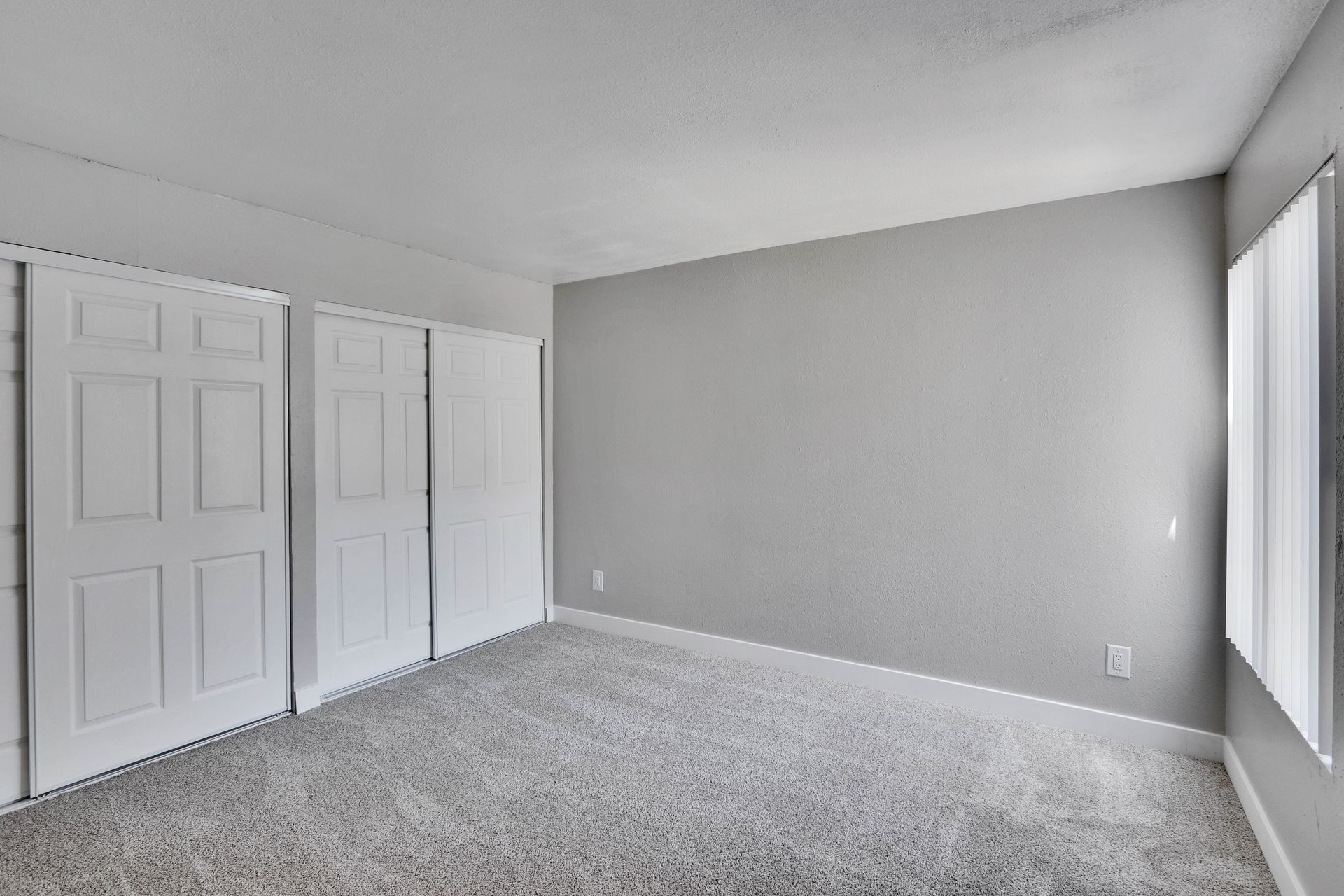 An empty room with a carpeted floor , white doors and windows.