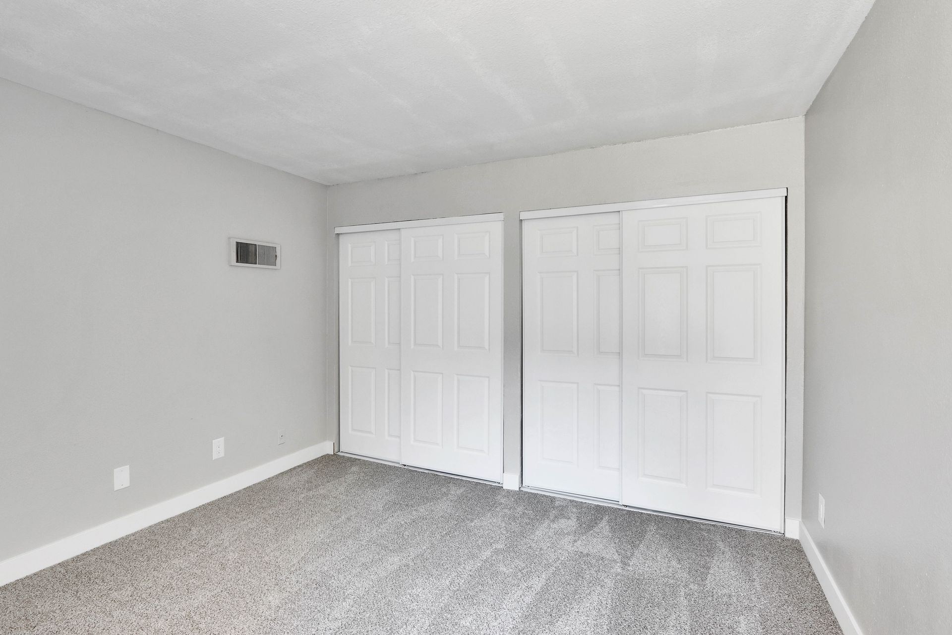 An empty bedroom with a carpeted floor and white closet doors.