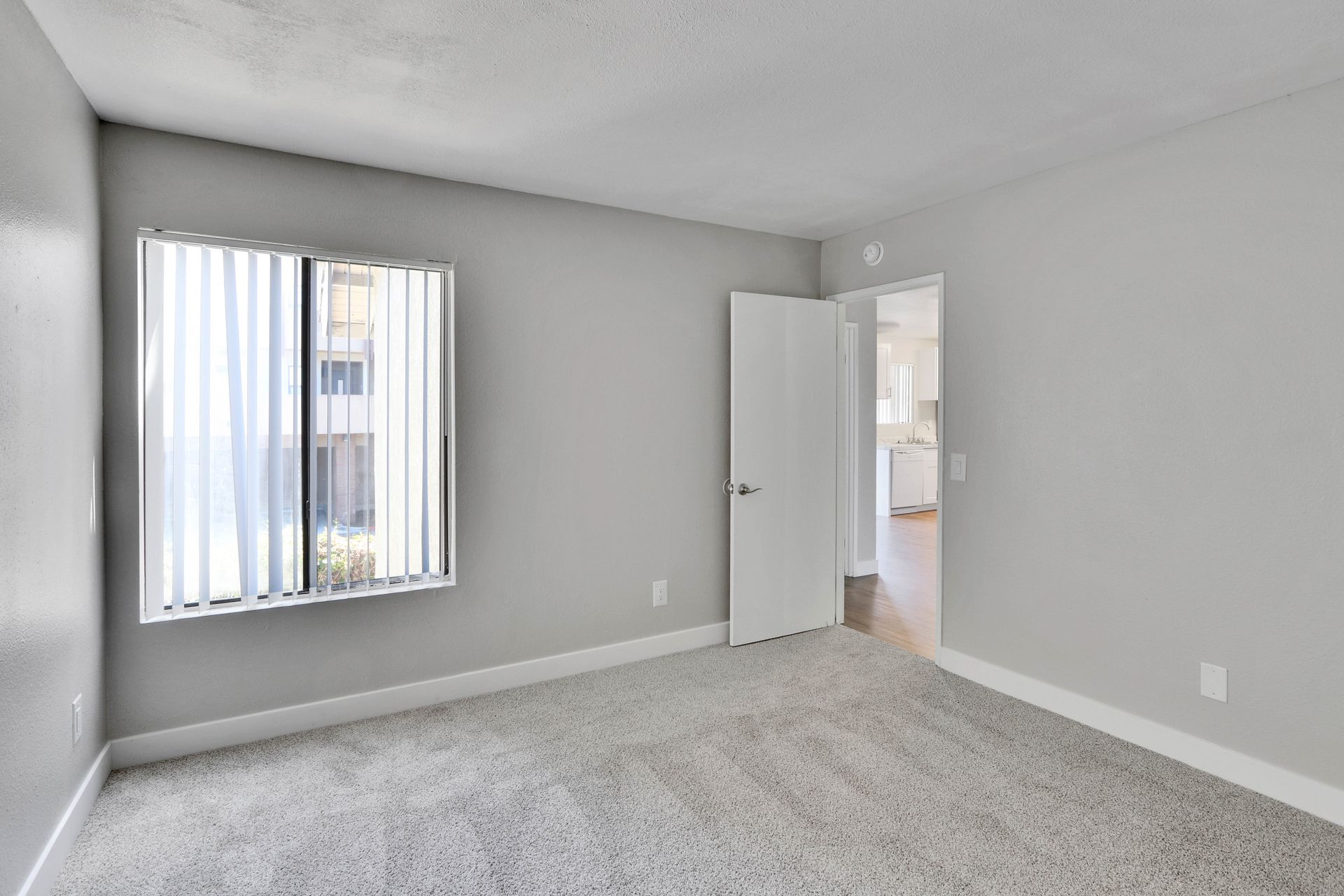 An empty bedroom with a window and a door.