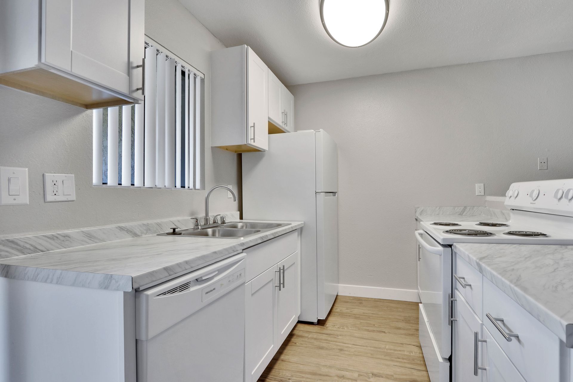 A kitchen with white cabinets , a stove , a refrigerator , and a sink.