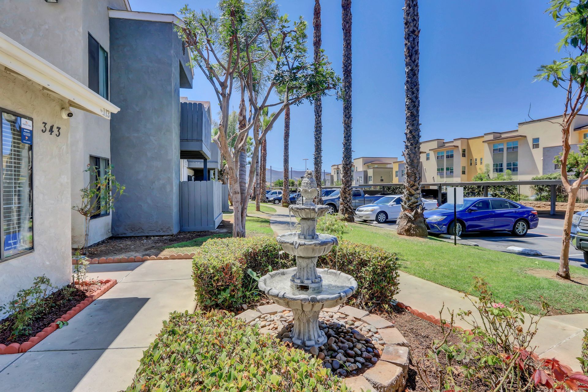 A fountain is in the middle of a garden in front of a building.