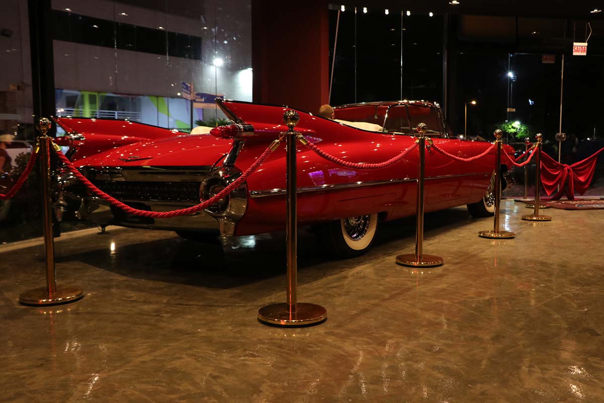 Um Cadillac conversível vermelho atrás de uma barreira de corda de veludo em um ambiente fechado.