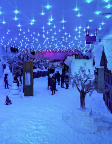 Parque de neve coberto com pessoas, prédios cobertos de neve, árvores e teto azul estrelado.