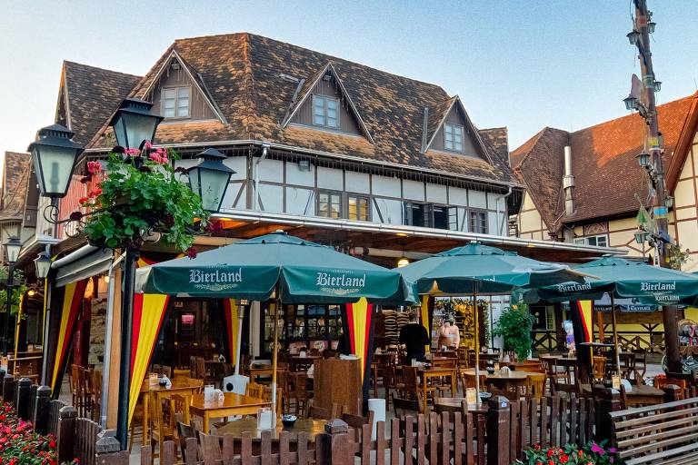 Restaurante ao ar livre com mesas sob guarda-sóis verdes, em frente a um edifício de enxaimel.