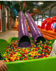 Dois toboáguas roxos desaguando em uma piscina de bolinhas verde cheia de bolas coloridas.