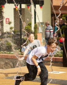Dois meninos brincando em uma fonte de água; correndo por riachos com expressões animadas.