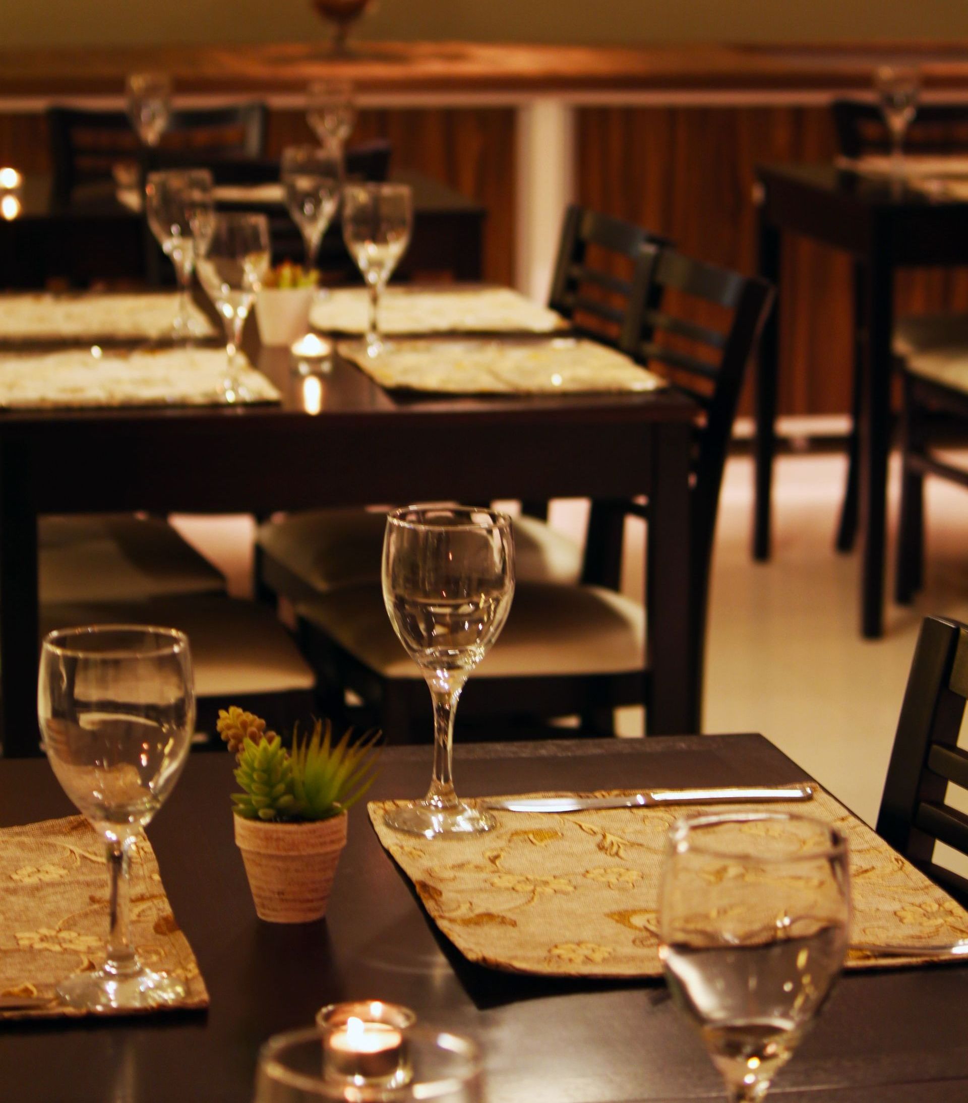 Interior do restaurante com mesas escuras, cadeiras e talheres prontos para os clientes.