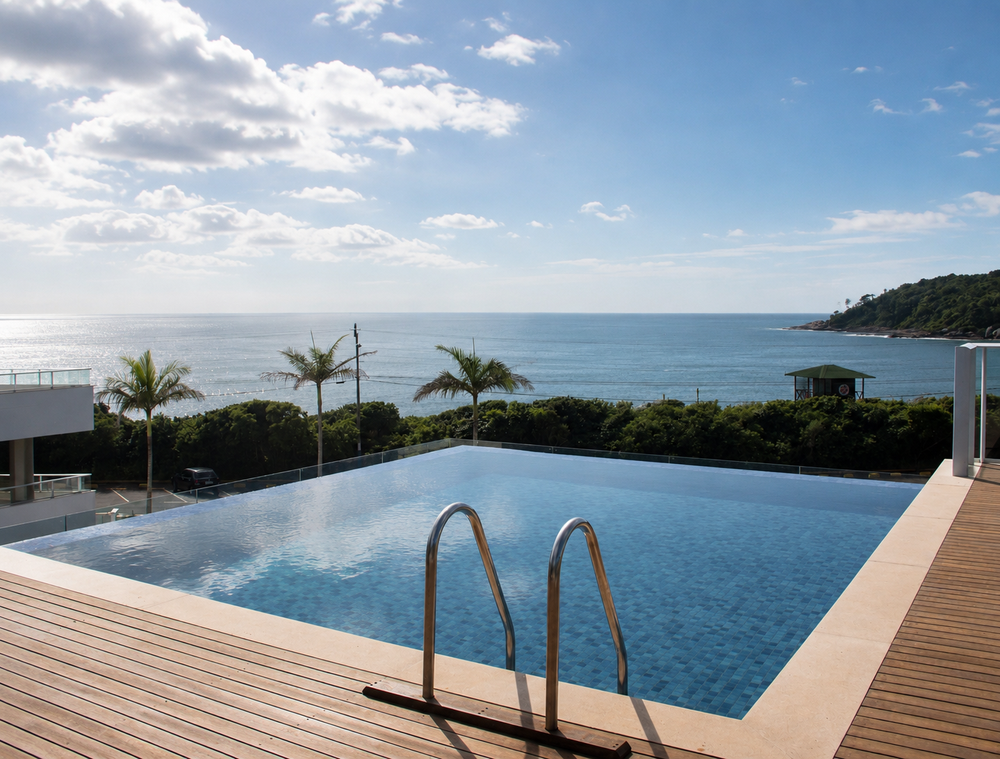 Piscina com vista para o mar. Palmeiras, água azul, deck de madeira.