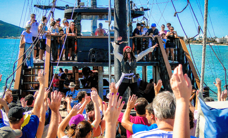 Pessoas em um navio pirata comemorando, artista fantasiado de Jack Sparrow, dia ensolarado na água.