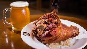 Joelho de porco assado em um prato com caneca de cerveja, sobre uma mesa de madeira.