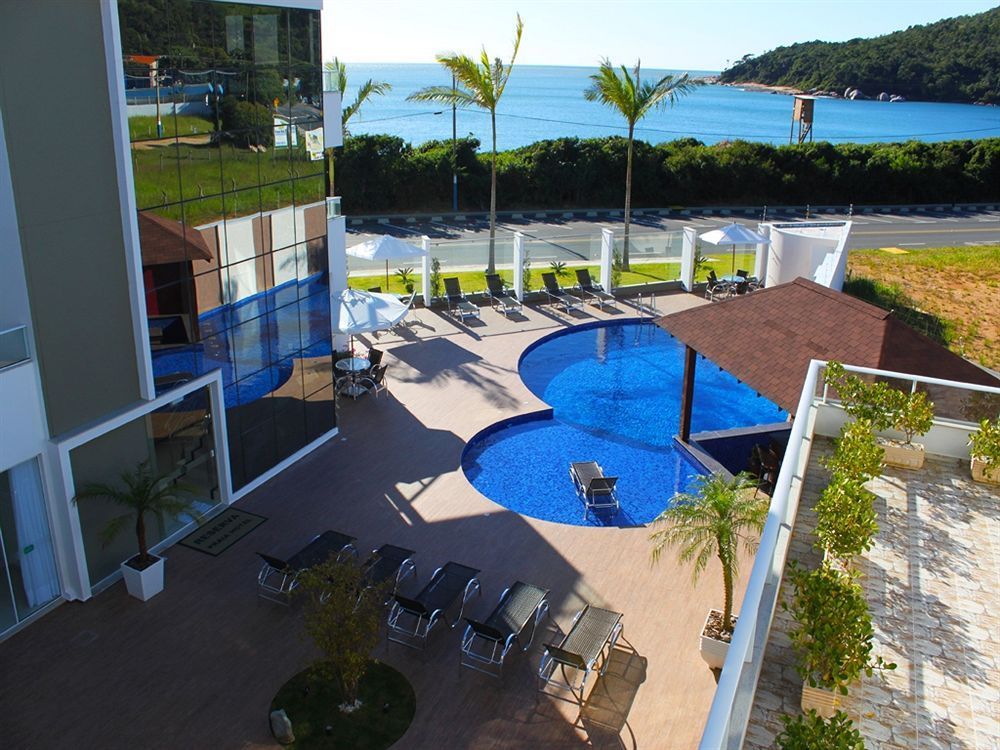 Hotel com piscina, vista para o mar. Piscina azul, palmeiras, espreguiçadeiras, dia ensolarado.