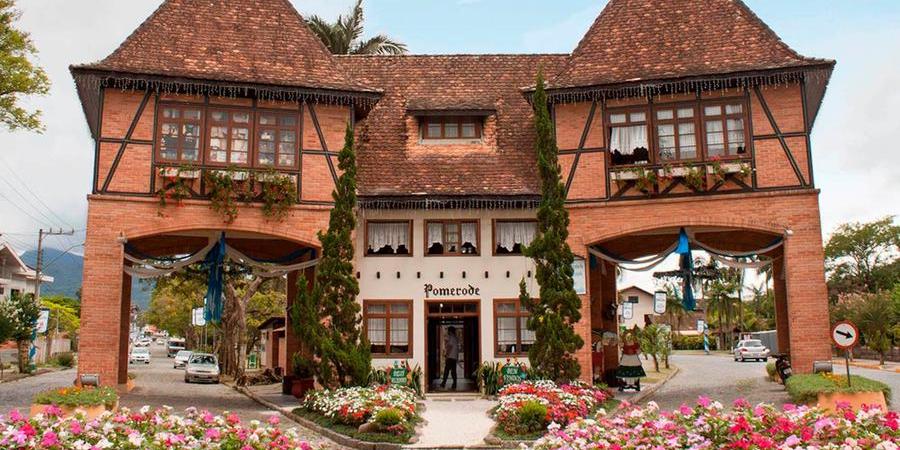 Um edifício de estilo europeu com tijolos, estrutura de madeira, passagens em arco e um jardim de flores em primeiro plano.