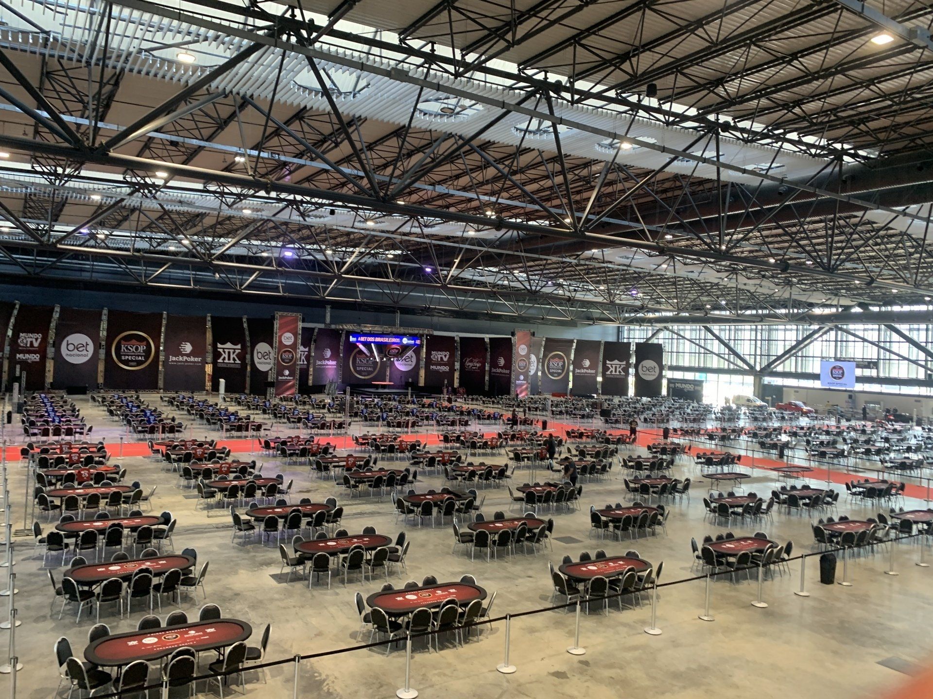 Grande salão com muitas mesas de pôquer preparadas para um torneio.