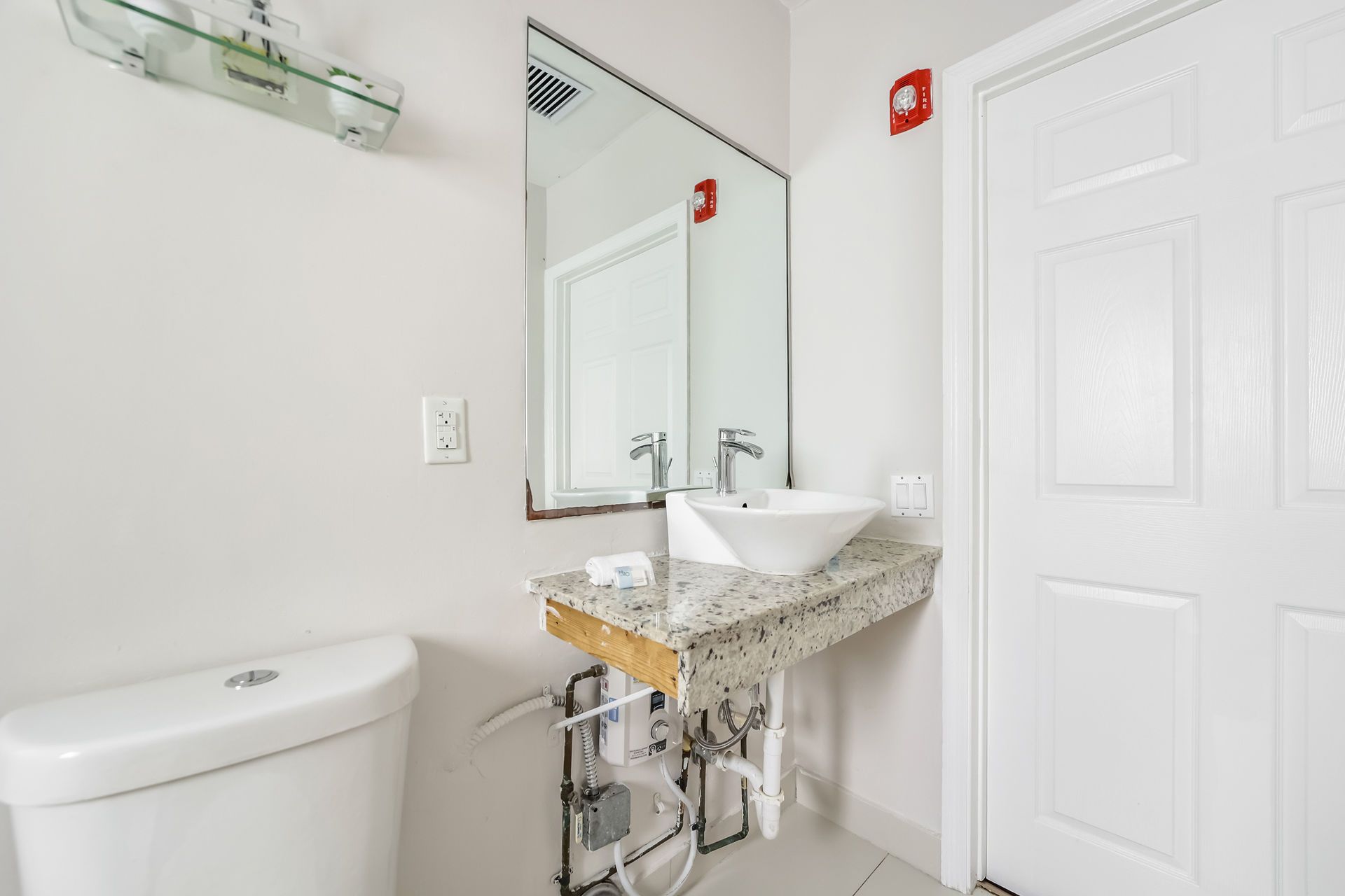 Bathroom with white toilet, sink with granite countertop, mirror, and white door.