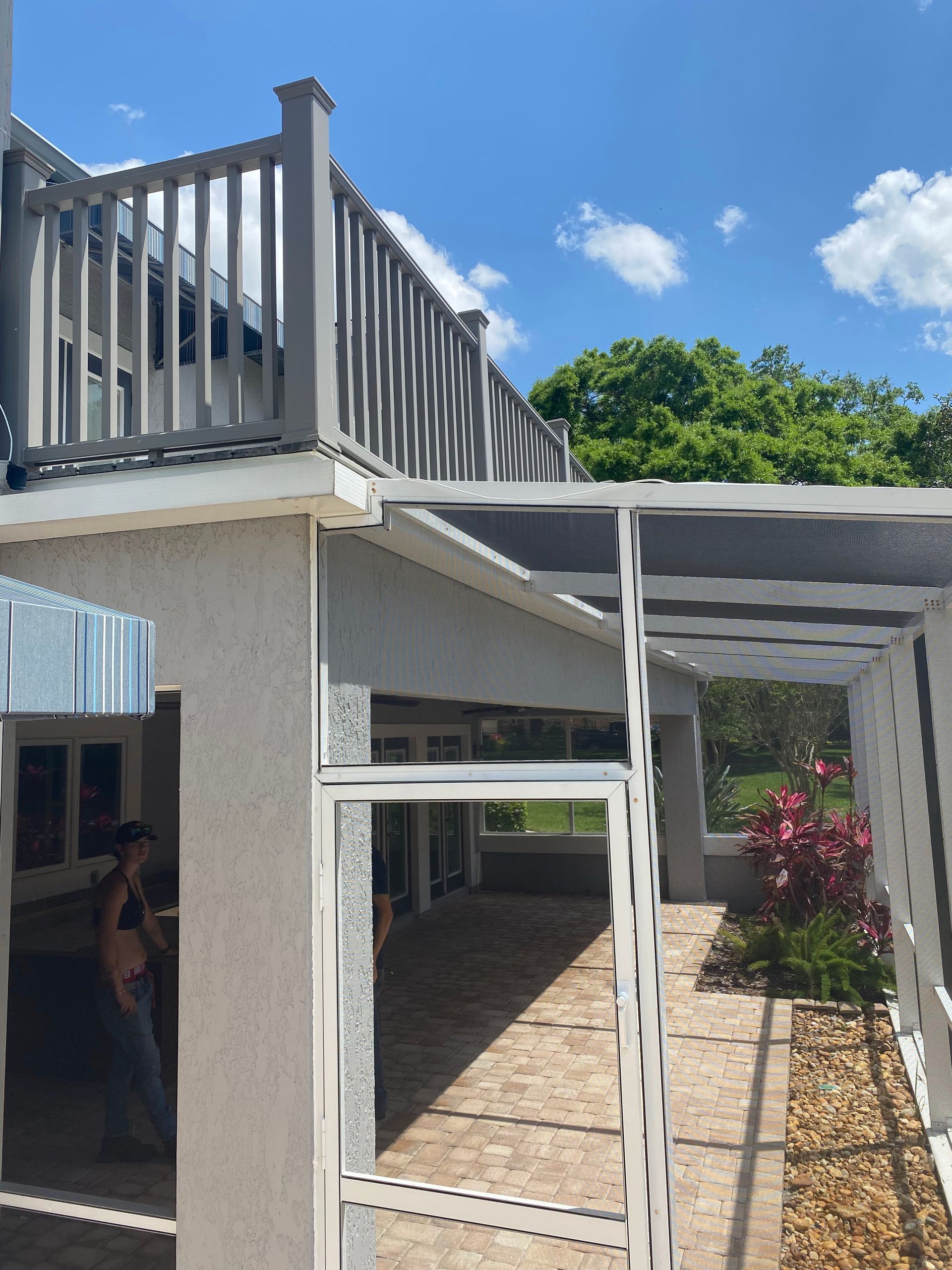 A building with a gray deck, white trellis, and a person standing near the patio in bright daylight.