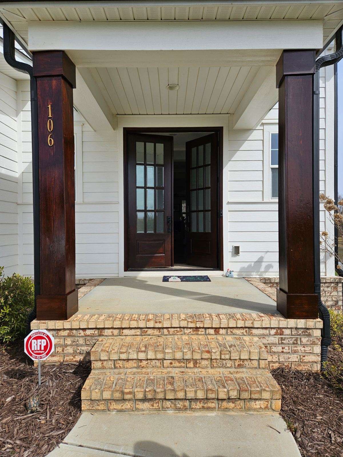Front porch with dark wood columns, brick steps, and double doors.