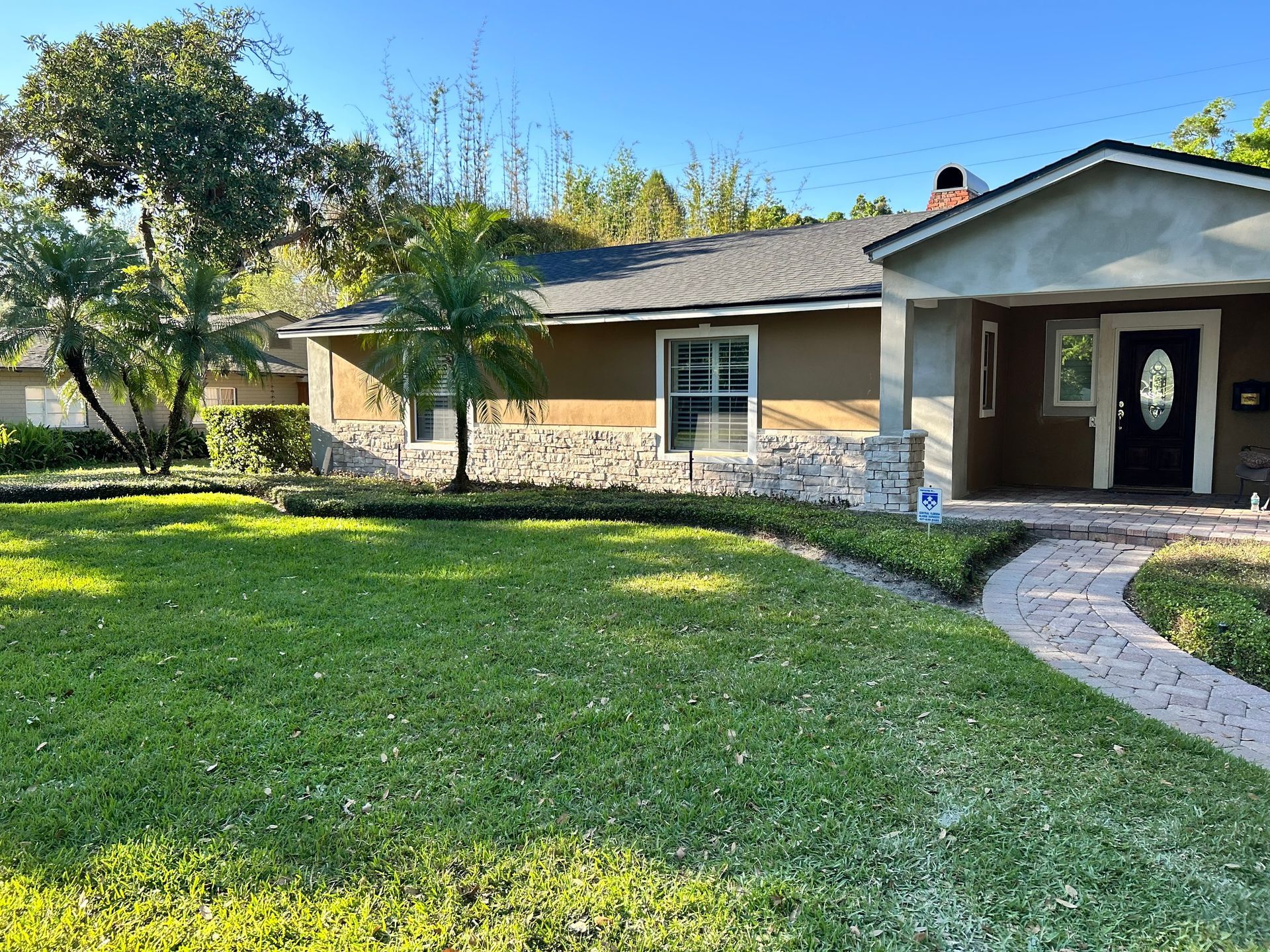 A single-story house with tan siding, stone accents, and a brick pathway leading to the front door.